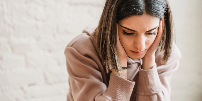 A photo of a young woman sitting with her elbows on her knees and her hands holding the sides of her face.